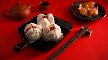Steamed red minced pork buns, fried shrimp dumplings, chopsticks and tea sets on a dining table. Chinese appetiser conceptの写真素材