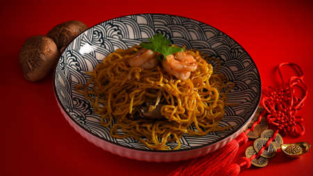 A tasty Chinese chow mein with shrimp on a porcelain plate, mushroom and Chinese lucky charms on red background.の写真素材