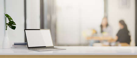 Laptop computer white screen mockup and a copy space on a modern white desk over blurred office background. 3d rendering, 3d illustrationの写真素材