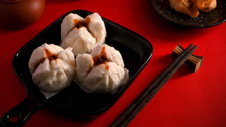 Steamed red minced pork buns on a plate and chopsticks on a dining table. Chinese appetiser conceptの写真素材