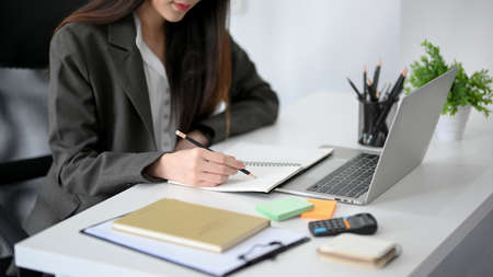 Closeup image of a beautiful businesswoman working at her office desk, writing on her personal book.の写真素材