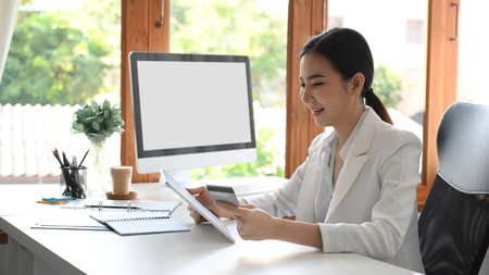 A successful female business owner or executive manager sitting at her office desk and transferring money via online application. credit card concept.の写真素材