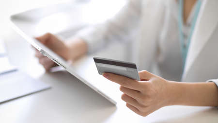 Cropped image of a businesswoman or female worker holding credit card and digital tablet computer at her desk.の写真素材