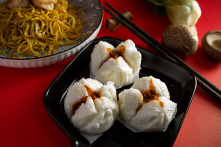 Yummy Chinese steamed bbq pork buns or red pork buns and chow mein noodles on a red dining table.の写真素材