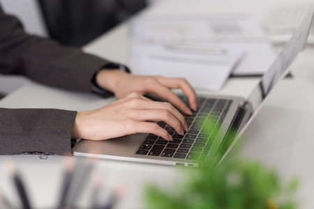 Close-up, side view image of a business woman or female's hands typing on laptop computer keyboard at her desk.の写真素材