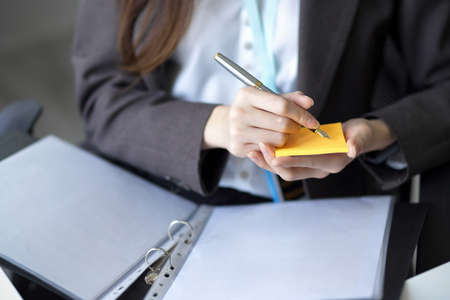 Cropped image of a Businesswoman taking a notes on sticky note while looking the informations on paperworks.の写真素材