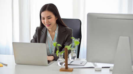 Beautiful asian female financial broker or accountant working on her portable laptop computer at her office desk.の写真素材
