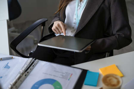 Cropped image of Attractive businesswoman using a digital tablet while sitting in modern office workspace.の写真素材