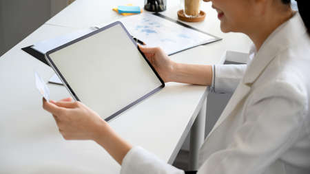 Cropped shot a a female executive manager holding credit card and smart digital tablet computer at her office desk. tablet blank screen, online money transaction.の写真素材