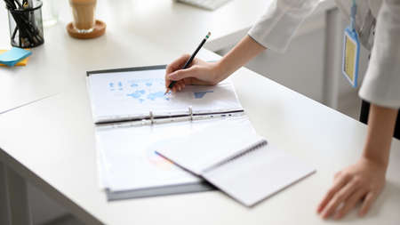 Cropped and close-up image of a business woman hands working or writing on financial data report on the office desk. Meeting, brainstorming or consulting.の写真素材