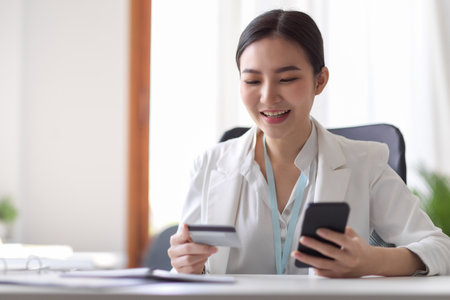 Elegant asian young business woman or entrepreneur holding smartphone and credit card at the desk. Businesspeople with credit card concept. Mobile banking, online shopping or Money transfering.の写真素材