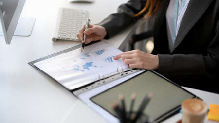 Cropped image of a businesswoman or financial manager sitting at her desk, reading and analysing a financial data report.  Financial report in a binder folder.の写真素材