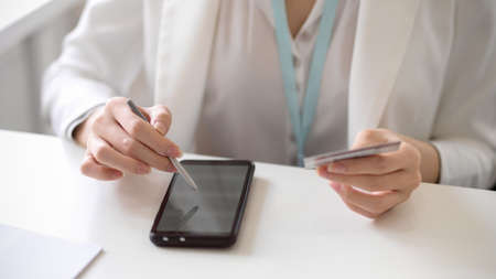 Cropped image of a female worker or businesswoman using stylus pen with smartphone, holding a credit card to connect her account with mobile application. Online payment concept.の写真素材