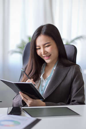 Portrait of an elegant female boss reading a book, checking some informations on a personal book, taking notes on her diary in the office.の写真素材