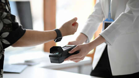 Cropped, close-up image of a man using his modern digital wristwatch paying his shopping. NFC...
