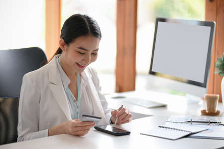 Female executive manager or business entrepreneur using mobile banking application to pay her bills, sitting in the modern office. credit card with smartphone.の写真素材