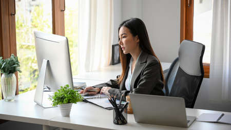 Focused business woman working desktop computer. Female employee pay attention on her project in the office. Female project manager concentrating on her marketing plans.の写真素材