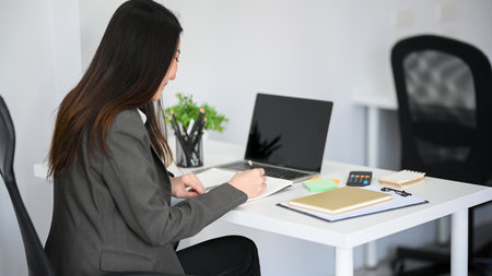 Asian young female employee sitting at her desk and working on her marketing assignment.の写真素材