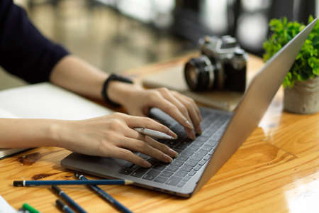 Cropped, closeup image of a female freelance photographer typing on laptop keyboard at her desk.
