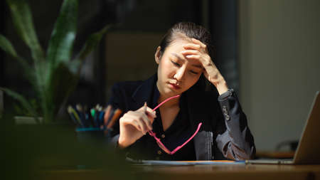 Stressed business woman working in the office. Headache, worried, overworked, unhappy, tired worker concept.の写真素材