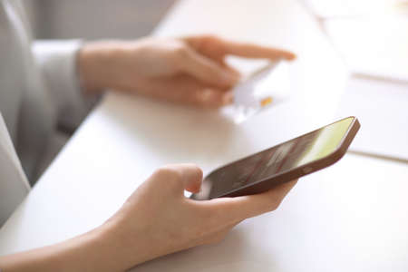 Close-up, a modern smartphone and credit card in female's hands on a desk. Mobile banking service, digital online payment concept.の写真素材