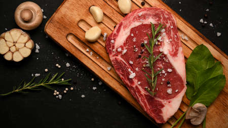 Top view of a raw marbled meat steak with seasoning and vegetables on a wooden plate. European food concept.の写真素材