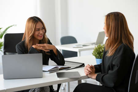 Successful Asian female manager talking with her marketing employee in modern office workplace.