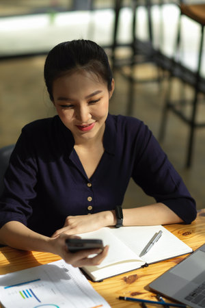 Portrait of a beautiful asian woman using smartphone at her office desk. Female chat, message, text with her friends.の写真素材