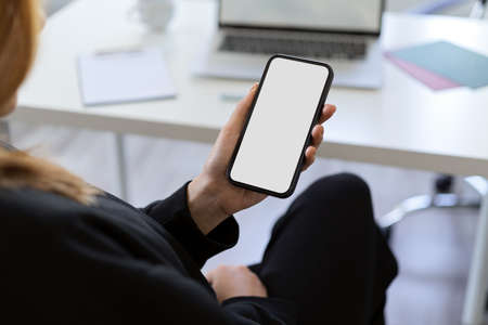 A female using a smartphone at her office desk. Smartphone or mobile phone blank screen mockup.