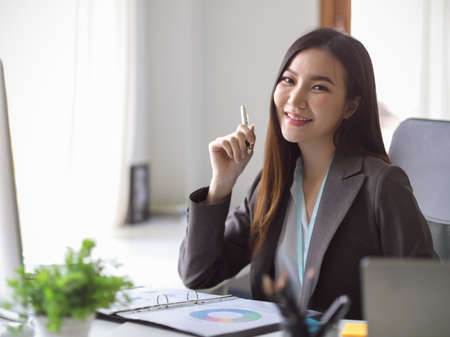 Beautiful and cheerful asian young businesswoman sitting at her desk with a smile face.