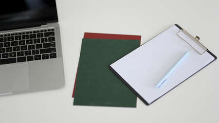 A notebook laptop computer, paper and clipboard paper with blank page on the worktable.