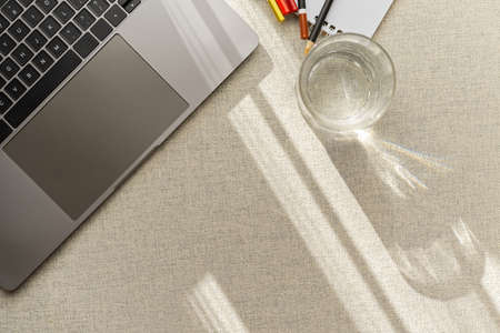 Cropped image, Top view of a simple workspace with portable laptop computer, a glass of water and stationery on table.の写真素材