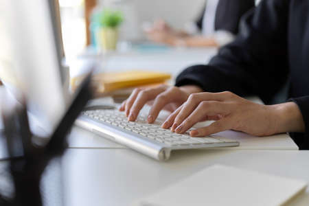 Cropped image of a worker working on pc computer, typing on keyboard, managing her online assignment in the office.の写真素材