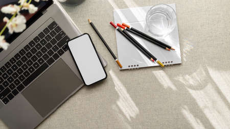 Close-up, top view or overhead view of a modern office desk with laptop computer, stationery and a smartphone blank screen mockup.の写真素材