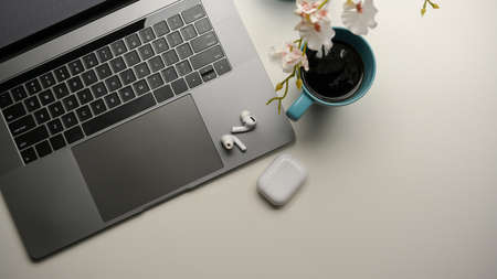 Top view of a simple modern workspace with laptop computer, earbuds and coffee cup on white table.の写真素材