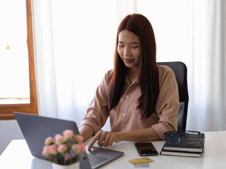an Asian young businesswoman or female worker using portable laptop computer or typing on notebook at her office.の写真素材