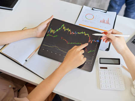 Top view of a financial analyst team analysing a stock market graph on digital tablet touchpad computer at their office desk.の写真素材