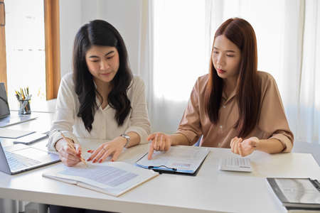 Beautiful businesswomen analysing and examining financial spreadsheet together in the office.の写真素材
