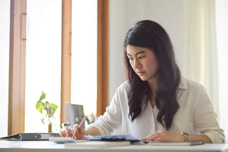 Young Asian female accountant or business entrepreneur working on her financial plans at her office.