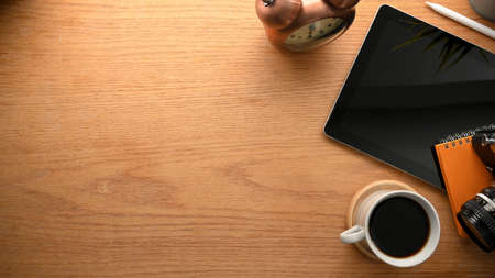 Top view of a worktable with tablet computer, coffee cup, stuff and copy space on wooden background.