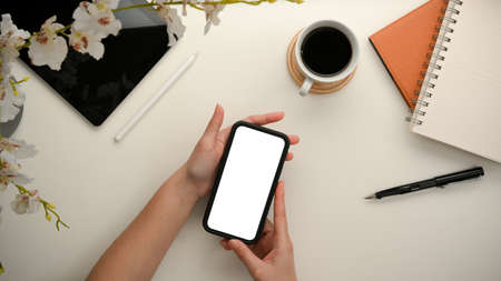 A girl's hands holding smartphone blank screen mockup on minimal workspace. top viewの写真素材