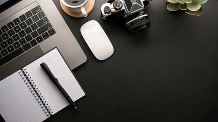 Modern hipster dark workspace with laptop computer, diary, camera, stuff and copy space on black background. top viewの写真素材