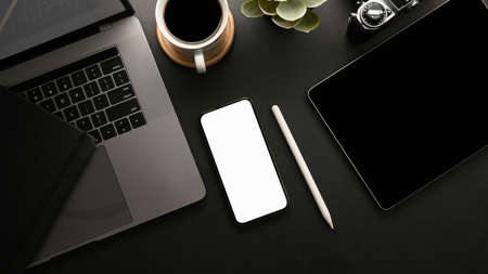 Modern dark workspace with digital devices and smartphone white screen mockup to show your graphic.の写真素材