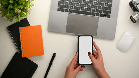 Top view, A female using smartphone on her modern office desk. phone blank screen mockup, laptop and supplies on table.の写真素材