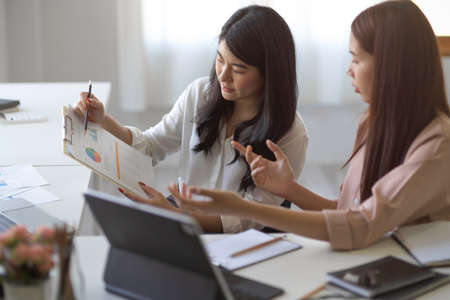 Two female colleagues focused on their market financial report graph chart on the papers in the office.の写真素材