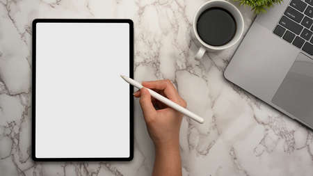 Close-up, top view of a female using stylus pen drawing on digital tablet touchpad computer on marble workspace.の写真素材