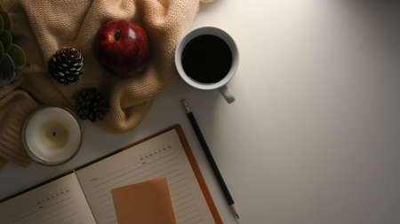 Cozy warm workspace with diary book, coffee mug, candle, sweater and decor on white table. top viewの写真素材