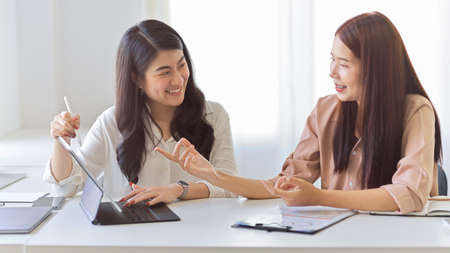 Smiling female worker talking, discussing work in office. Happy cheerful female employees chatting having a good relations.の写真素材