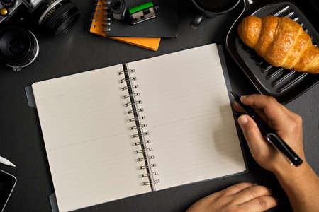 Top view, flat lay modern workspace on black background. A man taking notes on his diary book. Close-up hands image.の写真素材