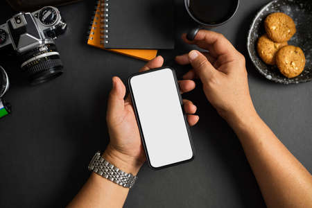 A man holding smartphone white screen mockup over his modern dark office desk.Top view, overheadの写真素材